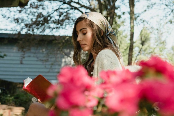 A woman reading a book with pink flowers in front